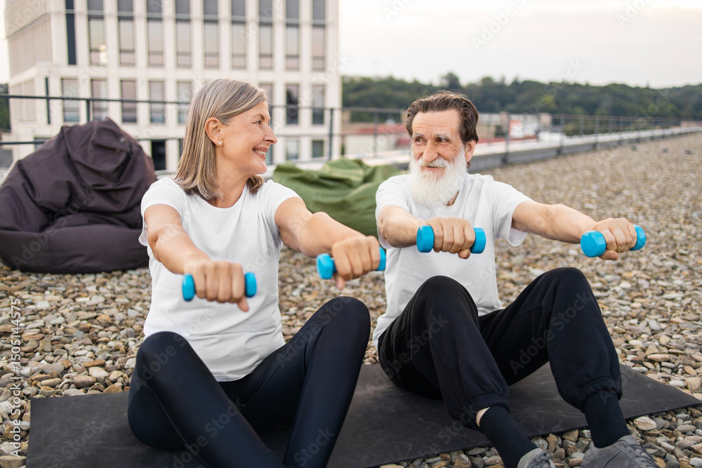 Fototapeta premium Senior man and woman practicing fitness with dumbbells outside on rooftop in urban setting