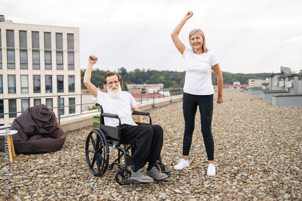 Obraz premium Elderly man in wheelchair and senior woman stretching arms together outdoors showcasing activity and fitness.