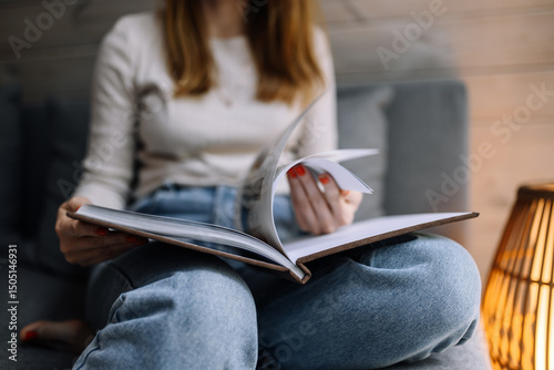 A woman sitting on a couch flipping through a magazine in a cozy home setting. A cozy creative moment captured in soft daylight.