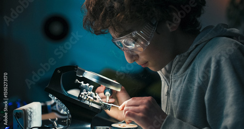A student spends his free time at a desk, learning electronics by soldering wires. He protects his eyes and concentrates as smoke rises from the repaired connection.