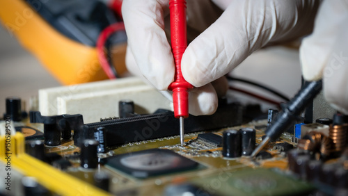 A person is working on a computer board with a red tool. The person is wearing gloves and he is focused on the task at hand