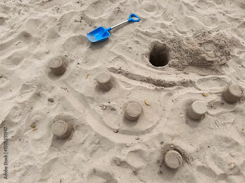 Sand towers on the beach with a blue shovel nearby and a deep hole