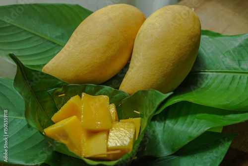 Fresh ripe mangoes and diced mango pieces served on green tropical leaves. A traditional Thai fruit display highlighting vibrant colors and natural, organic tropical produce.