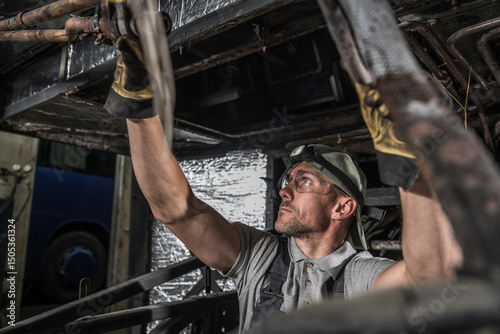 Mechanic Working on Vehicle Underside in Workshop With Tools and Focused Expression During Daylight Hours