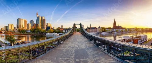 Obraz  z motywem Panoramic view of the old iron bridge Eiserner Steg crossing the Main river in Frankfurt, Germany, with the skyline behind during summer sunrise