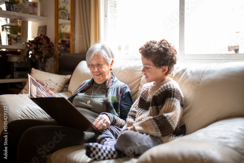 Bild auf Leinwand Grandmother showing family photo album to grandson on sofa