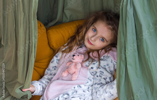 Beautiful little girl in comfortable clothes sits in children's room interior with knitted toy kigurumi in hands, selective focus