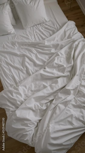 Unmade white bed with soft wrinkled sheets and pillows in top-down view, cozy minimalist bedroom interior with peaceful morning light and neutral color tones