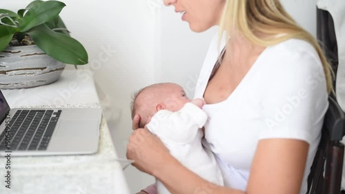 Mother-blonde in white T-shirt  works on computer  and holds baby in white overalls on hands. Newborn - happiness for family. New worries and lifestyle.
