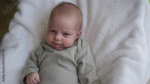 Baby with blue eyes in olive overalls lies on back. Close-up. First year of life and hygiene of child. Newborn - happiness for family. New worries and style life.