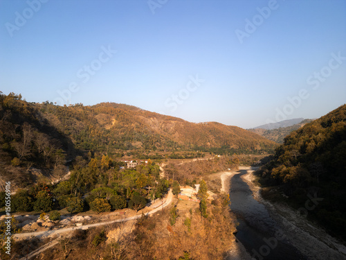 Aerial view of a mountain river winding through rocky terrain, illuminated by warm sunrise or sunset light. Majestic landscape captured from above with serene natural beauty.