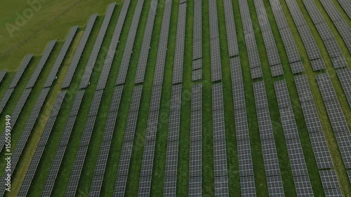 Top-down aerial shot showing long rows of solar panels on green grass fields in rural Poland near Chełmiec Mountain and Boguszów-Gorce