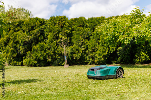Robotic lawn mower on green grass in a sunny garden, surrounded by trees and bushes. Ideal for concepts of smart gardening, automation, technology, and modern landscaping.