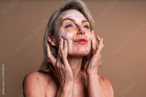 Beauty portrait of beautiful mature woman, concepts about cosmetics, skincare and wellness. Mature woman applying moisturizer on face for skincare and wellness