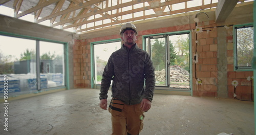 Construction worker with helmet walking through house under construction, observing progress, surrounded by exposed brick walls, wooden beams, and window frames