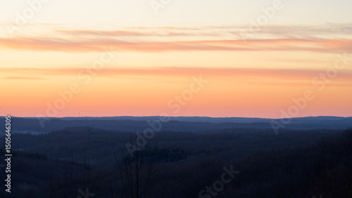 Vibrant colors fill the sky as the sun sets over distant hills, creating a peaceful atmosphere in the quiet landscape. This serene moment captures the beauty of nature.