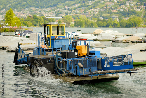 Fototapeta Harbor Garbage Removal Workboat Operating at Lakeside Marina with Scenic Hills