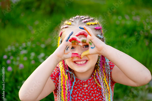 Cuadro en lienzo a joyful little girl shows her hands painted with bright colors in summer on a g