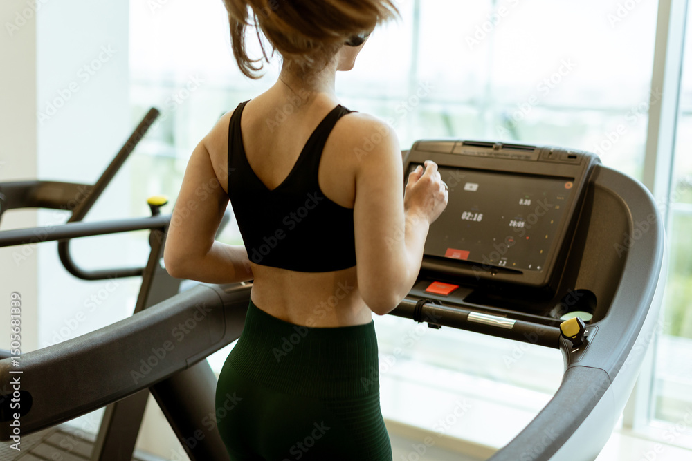 Fototapeta premium Jogging on a treadmill in a modern gym with large windows overlooking the city skyline in bright morning light
