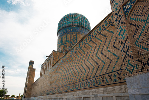 Ancient Islamic mausoleum in Samarkand with large turquoise dome and traditional ornamental tilework on brick walls, cultural heritage architecture of Central Asia with detailed geometric patterns photo