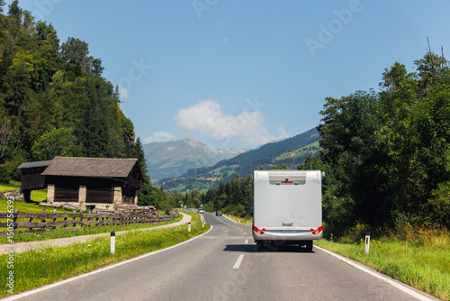 Scenic back view modern white family rv camper van vehicle drive Europe curvy road alpine pass mountain sunny summer day. Rving motorhome lifestyle travel adventure tourism trip Alps journey concept