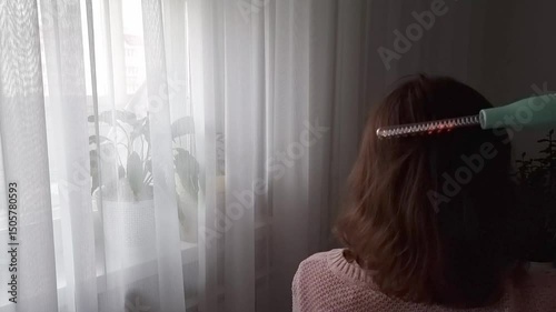 A woman runs a pulse massager through her hair, view from the back . Hair care at home with the Darsonval pulse massager.