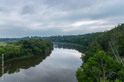 Peaceful landscape of the Grand River winding through lush green forest under a cloudy sky near Kitchener and Cambridge, Ontario, Canada.