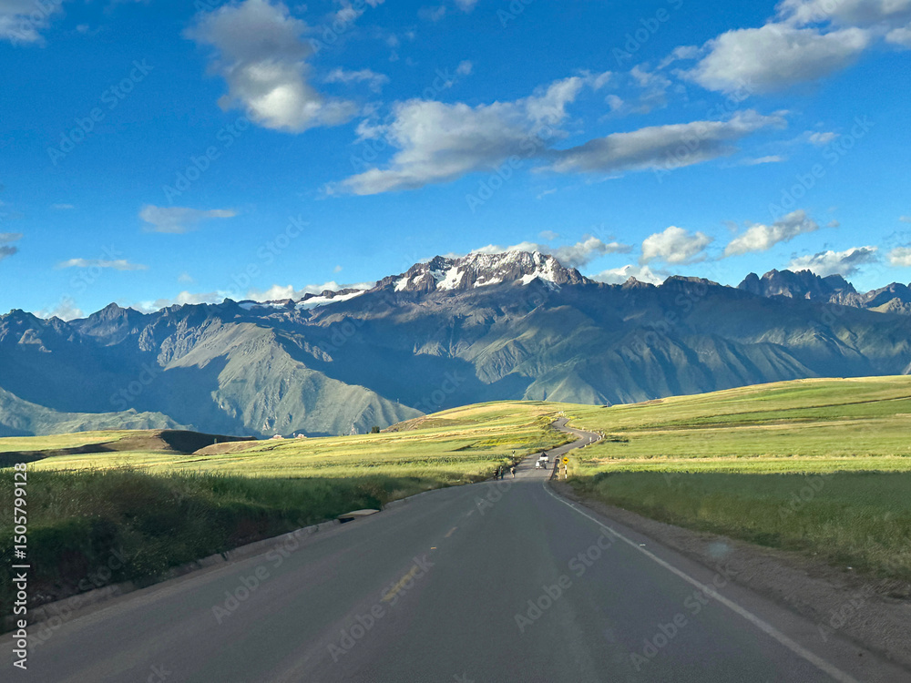 Naklejka premium A paved road zigzags through the undulations of the terrain, weaving between hills and valleys as it makes its steady ascent toward the rugged mountains of Peru. The black ribbon of asphalt contrasts 