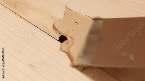 Wood knot cavity is poorly filled with putty, leaving gaps and air pockets, highlighting improper technique in floor repair process.