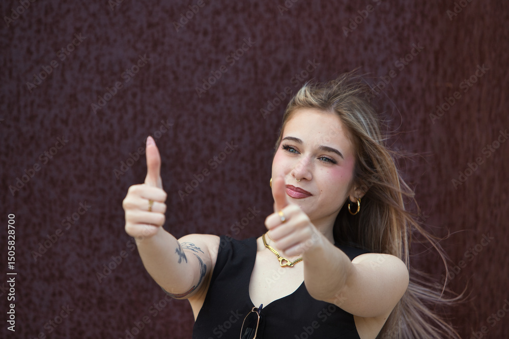 Fototapeta premium blonde woman with light eyes, young and beautiful, holds up the thumb of her two hands and makes a gesture that everything is fine, and it is correct. The woman is happy and smiles.