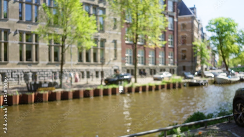 Fototapeta premium Blurred view of amsterdam's iconic canals with vintage architecture and trees reflecting a serene urban atmosphere.