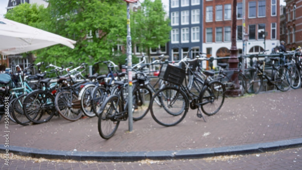 Fototapeta premium Blurred bicycles and canal scenery create a classic amsterdam vibe with defocused urban backdrop and vibrant greenery.