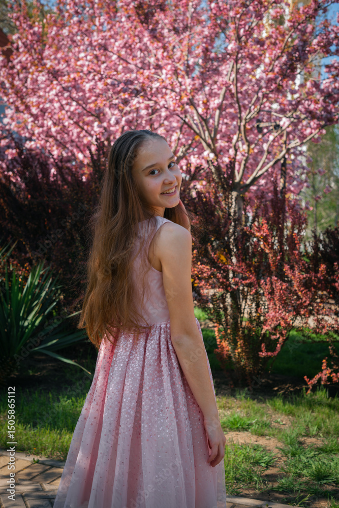 Young girl in a pink dress looking over her shoulder, standing near blooming cherry trees on a sunny spring day. Young girl in a pink dress looking over her shoulder, standing near blooming cherry trees on a sunny spring day.