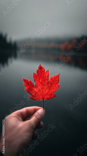 Vibrant Red Maple Leaf Held Above Calm Water Under Grey Skies During Fall