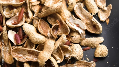 Empty peanut shells of peeled nuts falling on kitchen black plate. Organic waste compost component. Macro. Slow motion