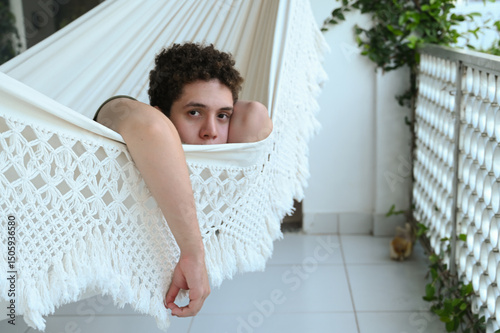 young man lying in hammock, man lying in hammock, looking at camera, white hammock

