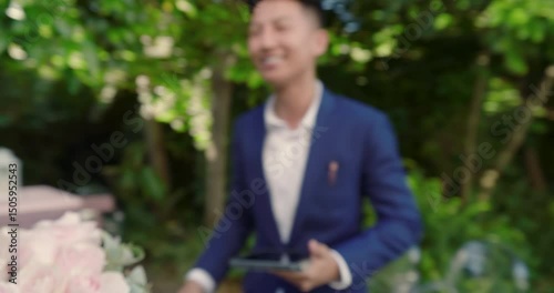 Asian officiant entering pink pergola starting wedding greeting couple while reading vows on tablet