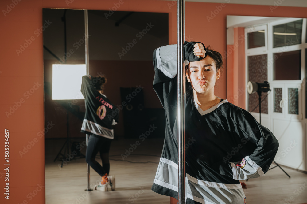 A confident woman stands playfully beside a pole in a studio, expressing joy and attitude through her pose. The scene is well-lit and combines an artistic and casual atmosphere. A confident woman stands playfully beside a pole in a studio, expressing joy and attitude through her pose. The scene is well-lit and combines an artistic and casual atmosphere.