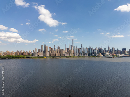City skyline view across the water, showcasing numerous buildings under a bright sky with scattered clouds, offering a scenic cityscape panorama.