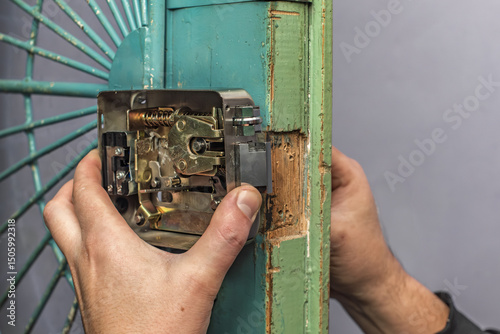 Closeup photo of male worker installing mortise lock. Hands fitting lock on gate, ensuring proper alignment and function