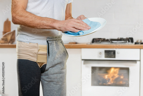 Fotografie Closeup photo of man wearing hernia bandage after operation doing dishwash at ki