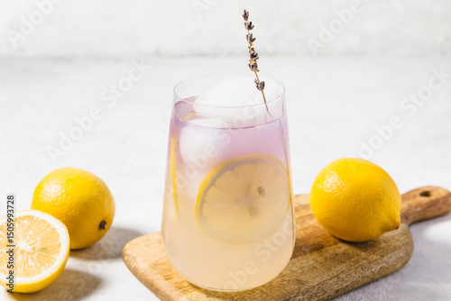 A refreshing lavender lemon lemonade served in a transparent glass filled with ice, garnished with a lemon slices. Summer drink and mocktail concept, natural organic lemonade recipe for holiday party.