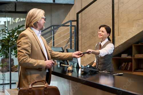 Fotografi Professional setting with businessman handing ID card to smiling receptionist at