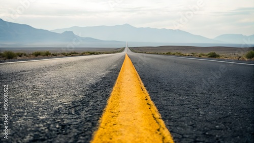 Long, straight asphalt road extending into a hazy desert landscape with mountains