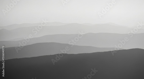 Horizontal panoramic view of rolling mountain ranges in grayscale, showcasing atmospheric perspective and tranquil natural landscape.