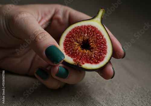 Woman with dark green matte manicure holding half of ripe fig
