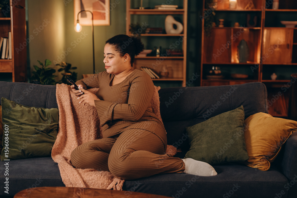 Obraz premium Happy mixed race woman reads message on smartphone sitting on sofa in living room
