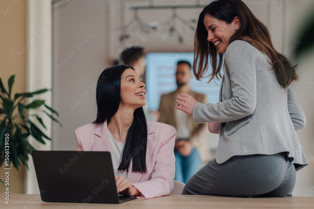 Businesswomen sharing a laugh while working on laptop in office Businesswomen sharing a laugh while working on laptop in office