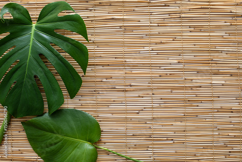flatlay of two monstera leaves on straw reed shade surface with a space for text