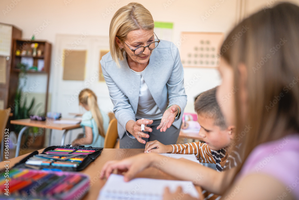 Fototapeta premium mature woman teacher checking school kids homework in the classroom
